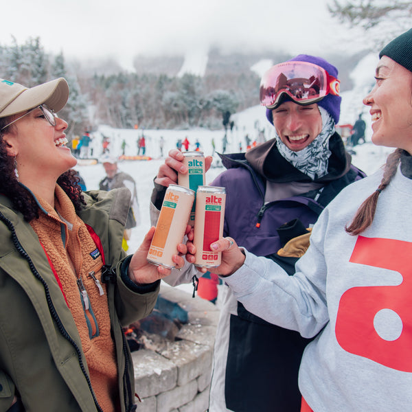 Three people at a snowy outdoor event, holding AlteBev drinks and smiling.
